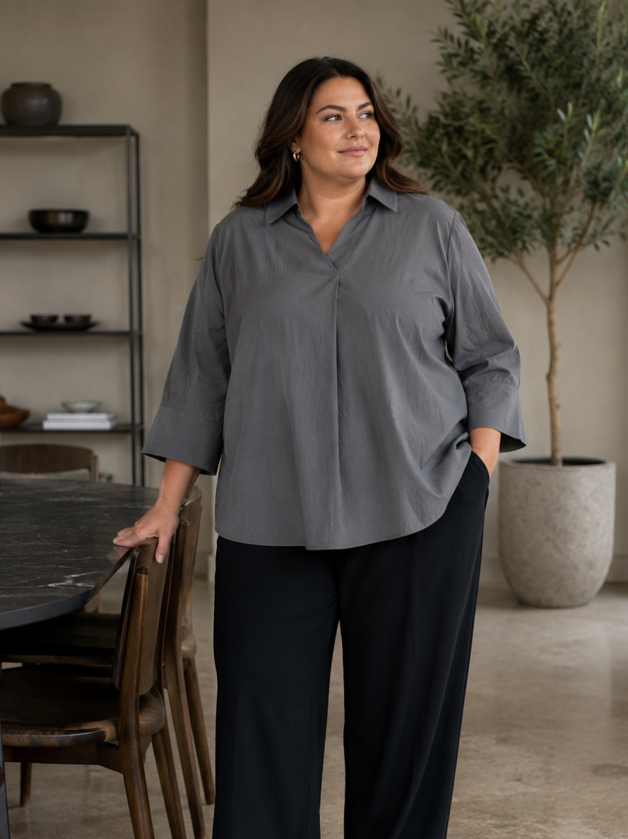 En plus size skjorte med krave, brede 3/4 ærmer. Den har en god længde og går ned og dækker det vi gerne vil ha' dækket. 

Billedet er genereret vha. AI.