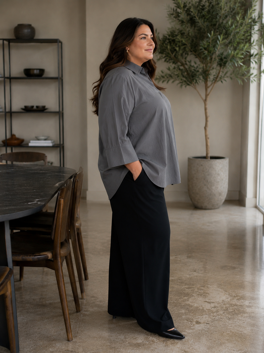 En plus size skjorte med krave, brede 3/4 ærmer. Den har en god længde og går ned og dækker det vi gerne vil ha' dækket. 

Billedet er genereret vha. AI.