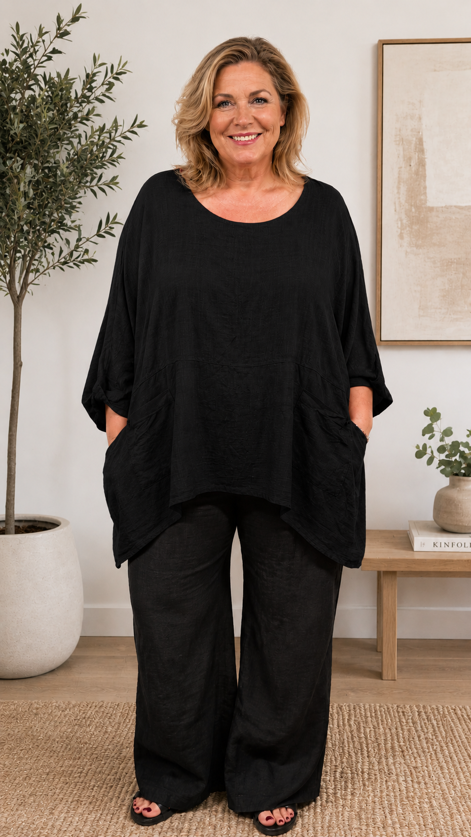 Kvinde i størrelse 46/48 iført Adler tunika som findes i flere farver. Tunikaen har en løs, oversized pasform med rund halsudskæring, 3/4-lange ærmer og store påsatte lommer foran. Den lette, strukturvævede kvalitet falder blødt over kroppen og giver et afslappet, komfortabelt look. Stylet efter din smag. Billed er Ai generet.
