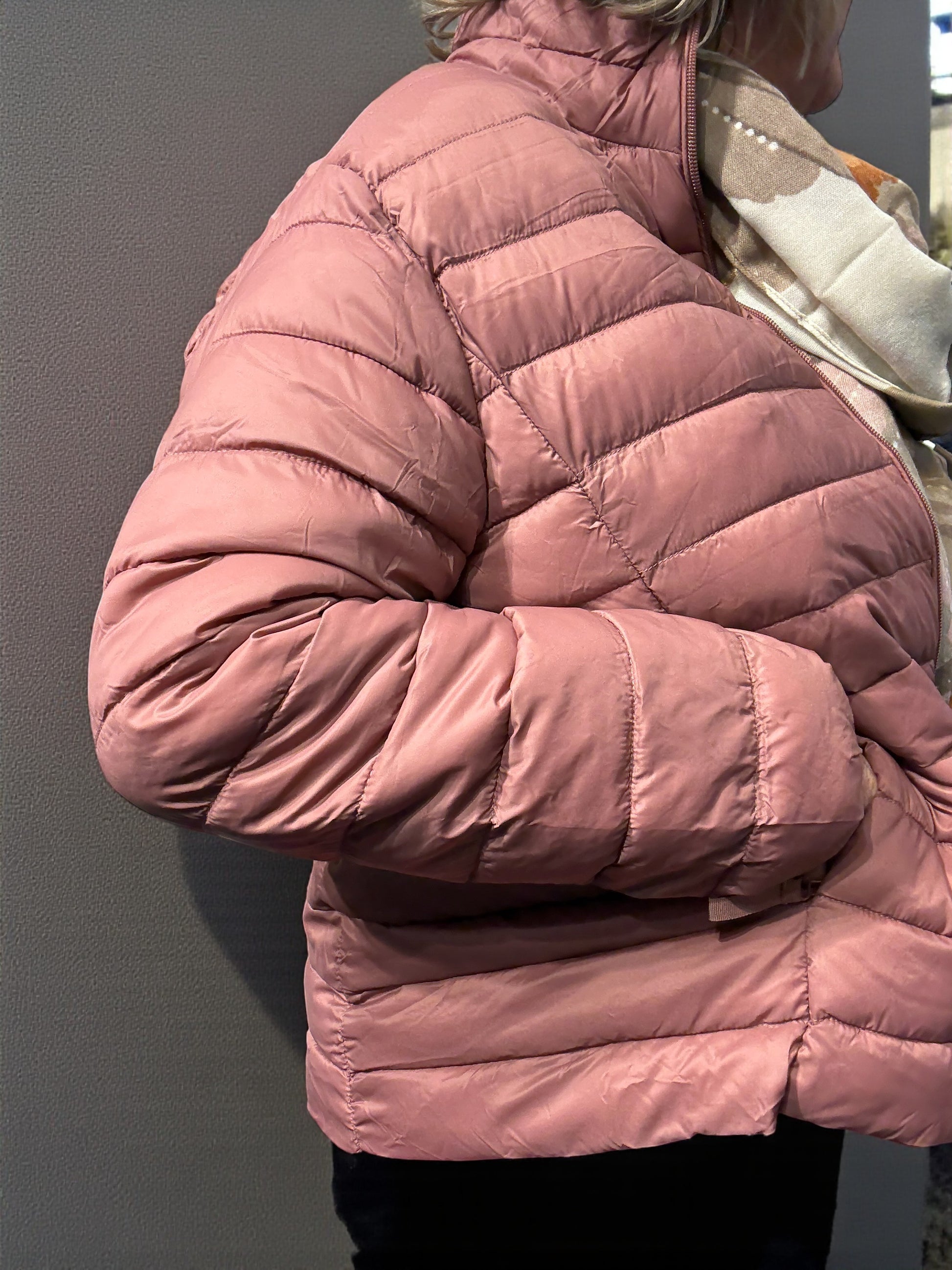 Jakken har høj hals, lange ærmer, lynlås foran og praktiske sidelommer med lynlås. Den er let foret med blød, syntetisk fyld, som giver god varme uden at virke tung.