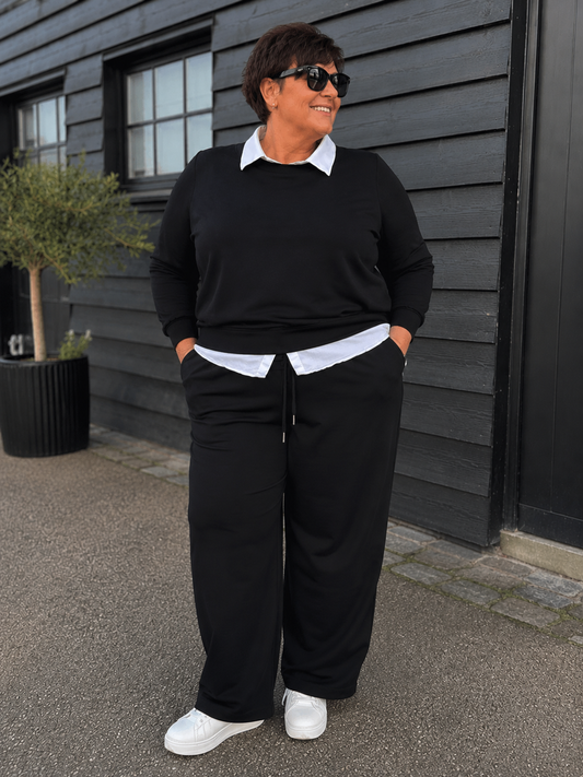 **Alt-tekst – Sabina 2 plussize buks (AI-genereret billede):**

AI-genereret billede af plus-size model i størrelse 50 iført sorte Sabina 2 bukser fra Wasabi. Bukserne har elastisk talje med bindebånd, lige brede ben og praktiske sidelommer. Modellen har bukserne stylet med en sort sweatshirt over en hvid skjorte og hvide sneakers.  en moderigtig viddebuks fantastisk pasform og komfortable look.