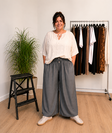 "Model i Tora viddebuks med bred smock-elastik i taljen, dekorative knapper og vide ben. Buksen vises i Grå sammen med en løs beige bluse. Modellen er str. 46/48 og 168 cm høj." Billed er ændret i Ai