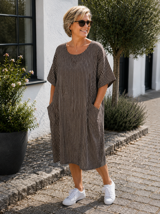 AI-genereret billede af Inga plussize bomuldskjole med klassiske striber, rund hals, korte ærmer og praktiske sidelommer. Kjolen vises på en plus-size model og er fremstillet i let bomuld.