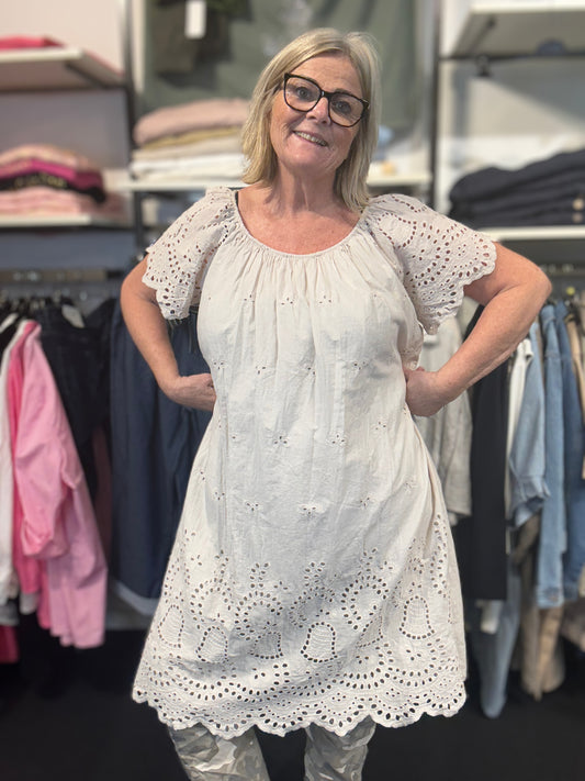 Sød og sommerlig kjole med broderingsdetaljer. Den har elastik i halsen, og er med korte ærmer. Den er i 100% bomuld. Her ses den i farven beige.