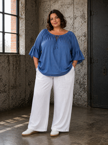 Joan er en skøn plussize tunika i blød tencel med et flot fald og en feminin pasform. Den brede elastiske halsudskæring med bindebånd og de fine flæseærmer giver tunikaen et elegant og afslappet udtryk, som passer perfekt til både hverdag og fest. billed er ai generet.