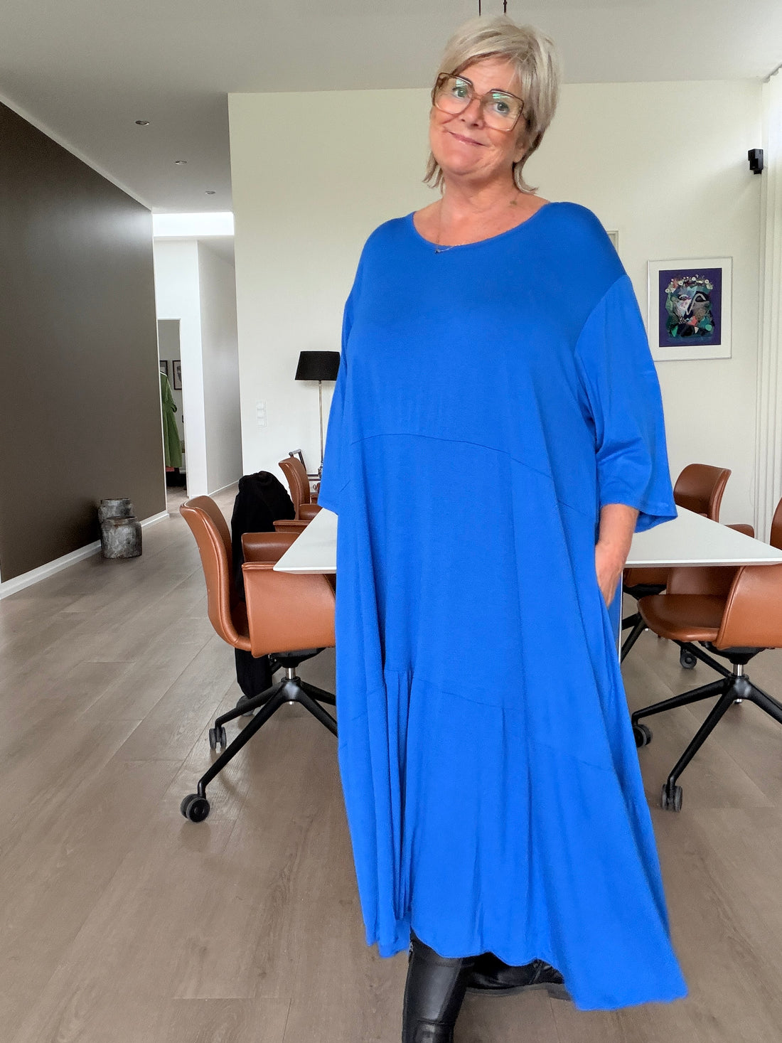 Tulle jersey kjole i plus size med flot, rummelig A-facon, rund hals og løse ærmer. Den bløde jersey falder smukt om kroppen og har et asymmetrisk snit med fine detaljer og god vidde. En smart og behagelig kjole til både hverdag og fest. Billedet er AI-genereret.