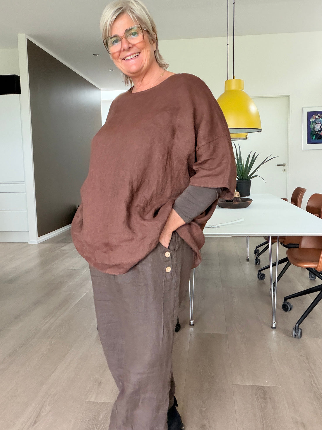 **Alt-tekst (AI-genereret billede)**

**AI-genereret inspirationsbillede af Linda hør tunika. Tunikaen har en løs og rummelig pasform med rund hals, korte ærmer og et flot, enkelt design i 100 % hør. Stylet med jeans på en plus-size model i et råt industrilokale. Fås i mange farver.
