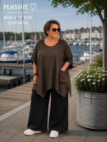 Lena Plus Size tunika i blød og let kvalitet med en flot, afslappet pasform. Tunikaen har rund hals, korte ærmer med opsmøg, praktiske lommer og en asymmetrisk kant, der falder smukt. Den løse facon gør den behagelig at have på og nem at style med både bukser, shorts og leggings. Fås i flere flotte farver og passer perfekt til plus size kvinder, der ønsker komfort og moderne stil.ai generet billed.