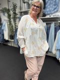 Smuk plus size bluse fra Sigensgaard med broderede guld blomster. Den er i 100% bomuld, som gerne må se lidt krøllet ud. Den har v-hals, lange ærmer som kan smøges op grundet knapåbning ved ærmets afslutning. Her ses den i en flot hvid.