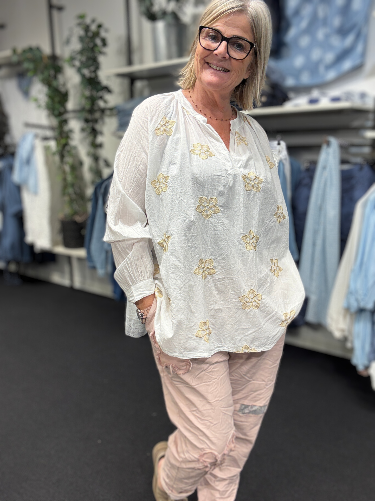 Smuk plus size bluse fra Sigensgaard med broderede guld blomster. Den er i 100% bomuld, som gerne må se lidt krøllet ud. Den har v-hals, lange ærmer som kan smøges op grundet knapåbning ved ærmets afslutning. Her ses den i en flot hvid.