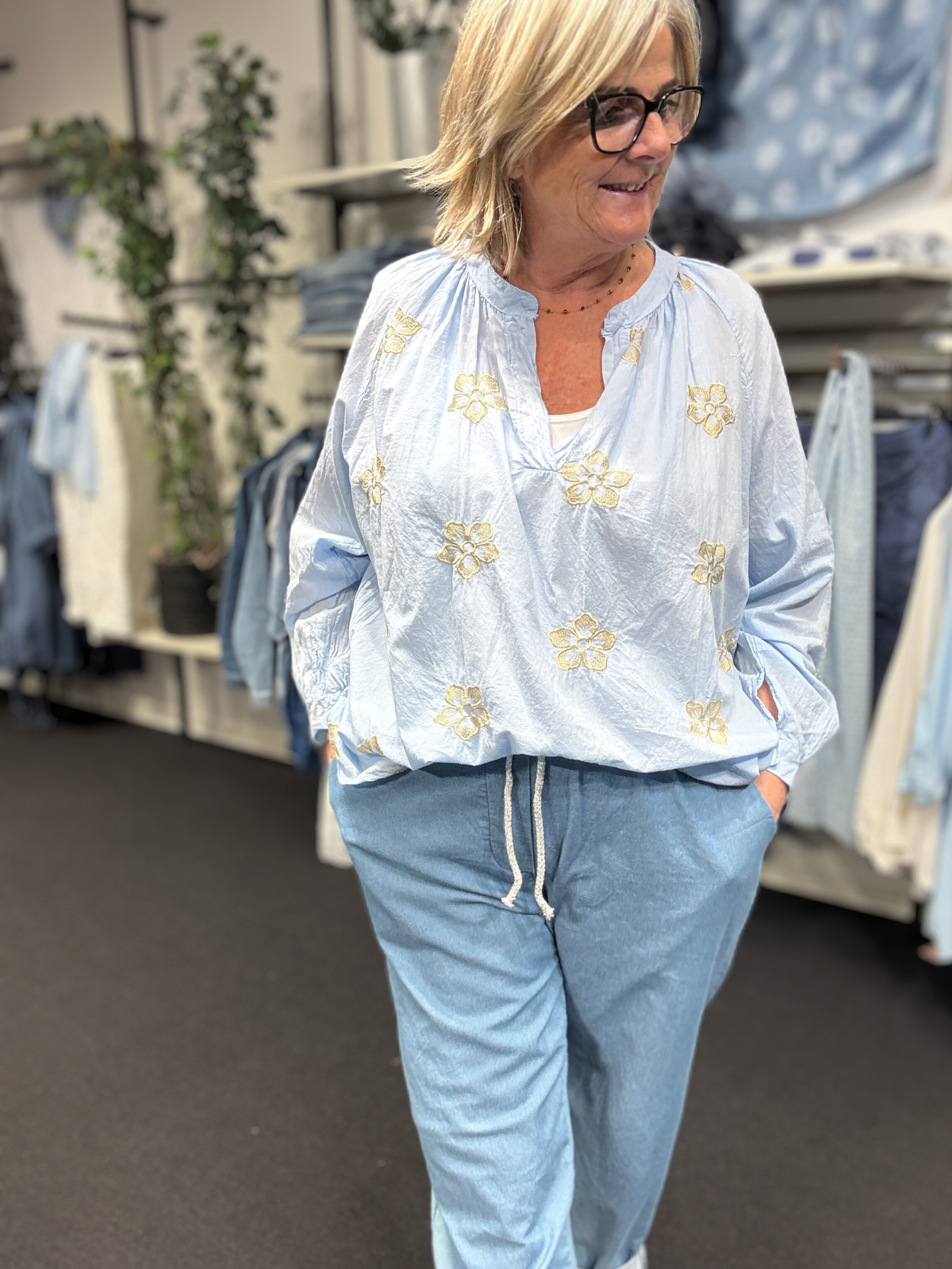 Smuk plus size bluse fra Sigensgaard med broderede guld blomster. Den er i 100% bomuld, som gerne må se lidt krøllet ud. Den har v-hals, lange ærmer som kan smøges op grundet knapåbning ved ærmets afslutning. Her ses den i en flot lys blå farve.