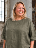 **AI-genereret inspirationsbillede af Linda hør tunika. Tunikaen har en løs og rummelig pasform med rund hals, korte ærmer og et flot, enkelt design i 100 % hør. Stylet med jeans på en plus-size model i et råt industrilokale. Fås i mange farver.