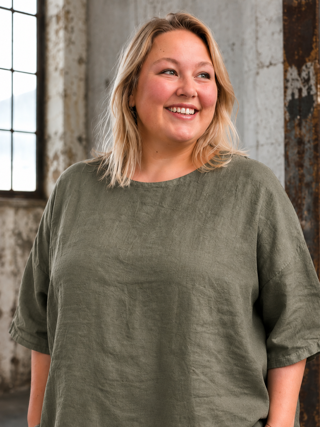 **AI-genereret inspirationsbillede af Linda hør tunika. Tunikaen har en løs og rummelig pasform med rund hals, korte ærmer og et flot, enkelt design i 100 % hør. Stylet med jeans på en plus-size model i et råt industrilokale. Fås i mange farver.