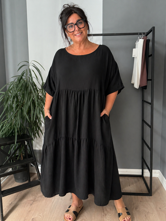 “Lolli kjole i ensfarvet – løs og luftig kjole i midi længde med korte ærmer og rund hals. Kjolen har en afslappet pasform med let rynk under brystet, der giver et feminint fald. Fremstillet i let materiale, perfekt til hverdagsbrug og komfort billed er Ai generet.