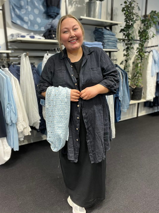 Smuk plus size tunika i den lækreste hør kvalitet. Den er i a-facon, som gør, at den er klædelig til de fleste pluspiger. 7/8 dels ærmer med elevatorhejs. Tunikaen kan bruges både åben og lukket. Her ses den i den flotte marine.