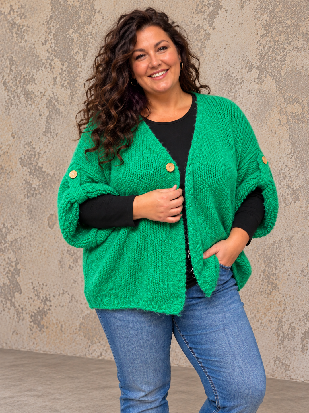 Mona plussize cardigan i chunky strik, stylet i et afslappet look mod en rå, rustik baggrund.
Billedet er ai-genereret.