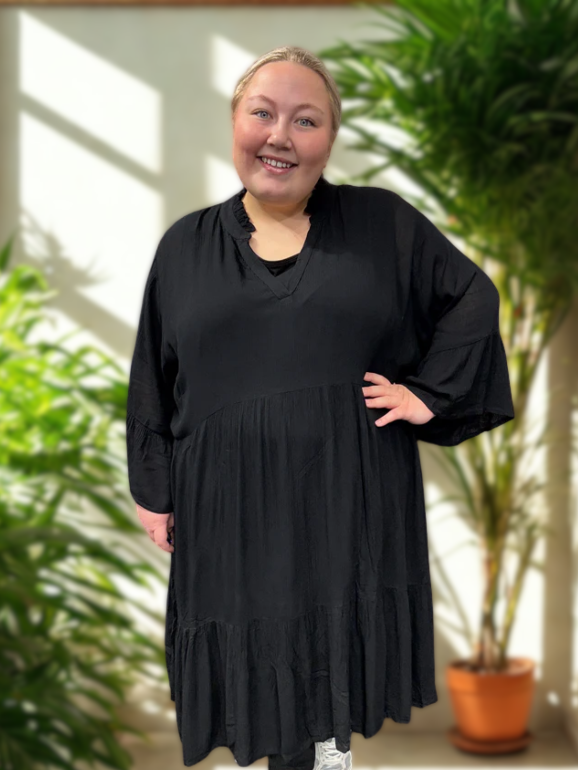 Pyntet sort kjole som er i en god facon til plussize kvinder. Den er fra mærket Kaffe Curve, og modellen på billedet bruger en str. 54. 

*Baggrunden på billedet er AI-genereret