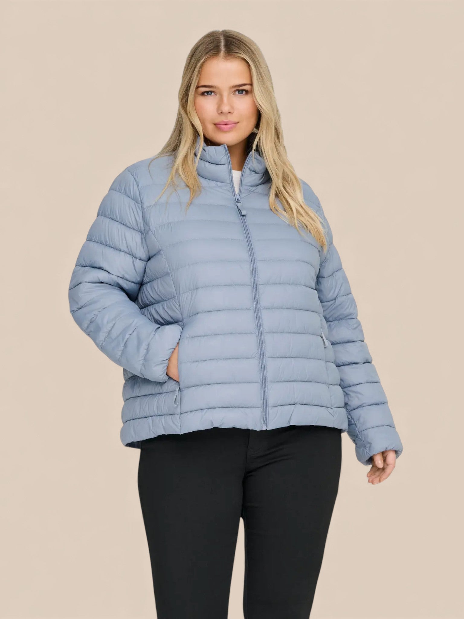 Jakken har høj hals, lange ærmer, lynlås foran og praktiske sidelommer med lynlås. Den er let foret med blød, syntetisk fyld, som giver god varme uden at virke tung.