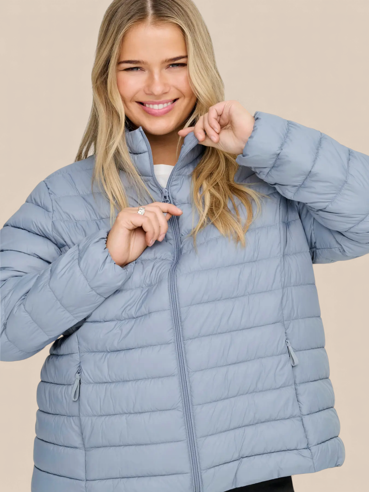 Jakken har høj hals, lange ærmer, lynlås foran og praktiske sidelommer med lynlås. Den er let foret med blød, syntetisk fyld, som giver god varme uden at virke tung.