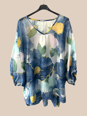 Denne smukke tunika er lavet i 100% tencel, og er udsmykket med store blå blomster. Den har et bredt elastikstykke ved ærmet afslutning, og så er den med v-hals. 