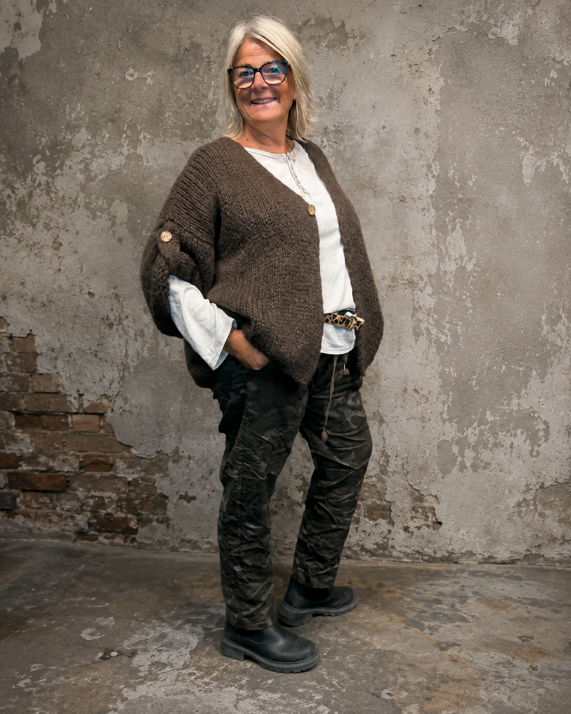 Mona plussize cardigan i chunky strik, stylet i et afslappet look mod en rå, rustik baggrund.
billed er ai generet