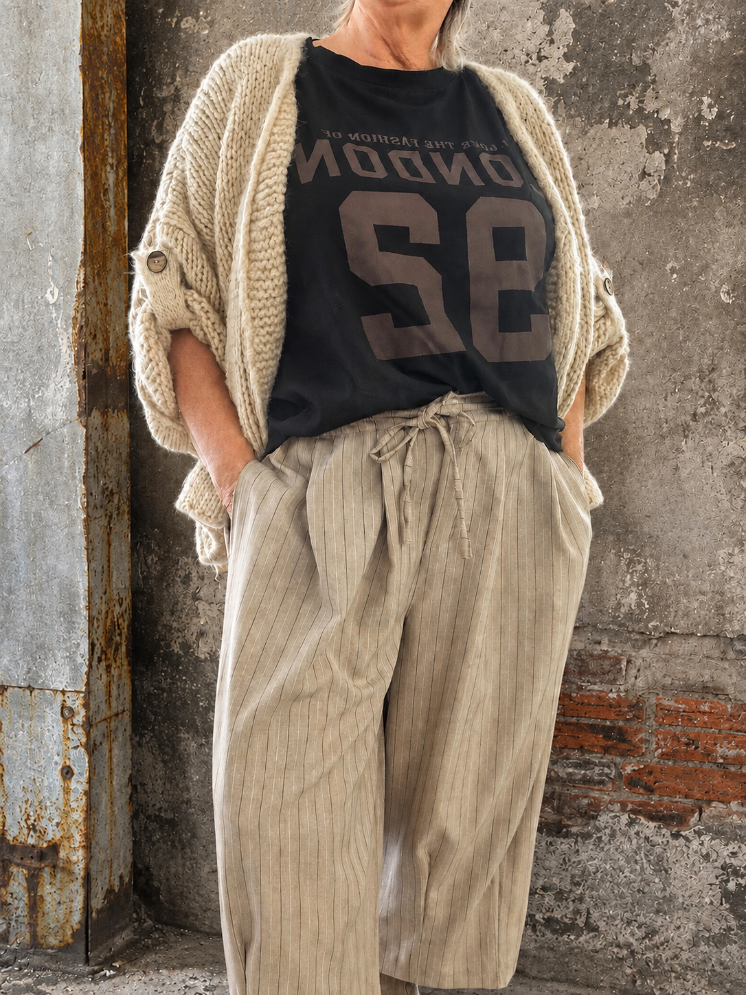 Mona plussize cardigan i chunky strik, stylet i et afslappet look mod en rå, rustik baggrund.
