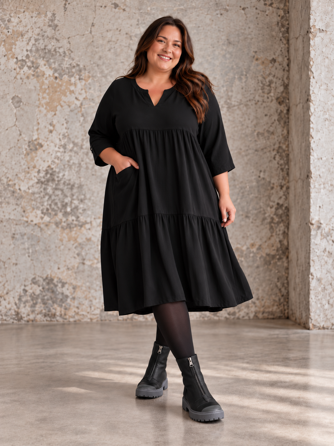 "Rigmor plussize-kjole med flot A-facon, flere lette lag, forlænget ryg og to diskret placerede lommer foran, der virker slankende."