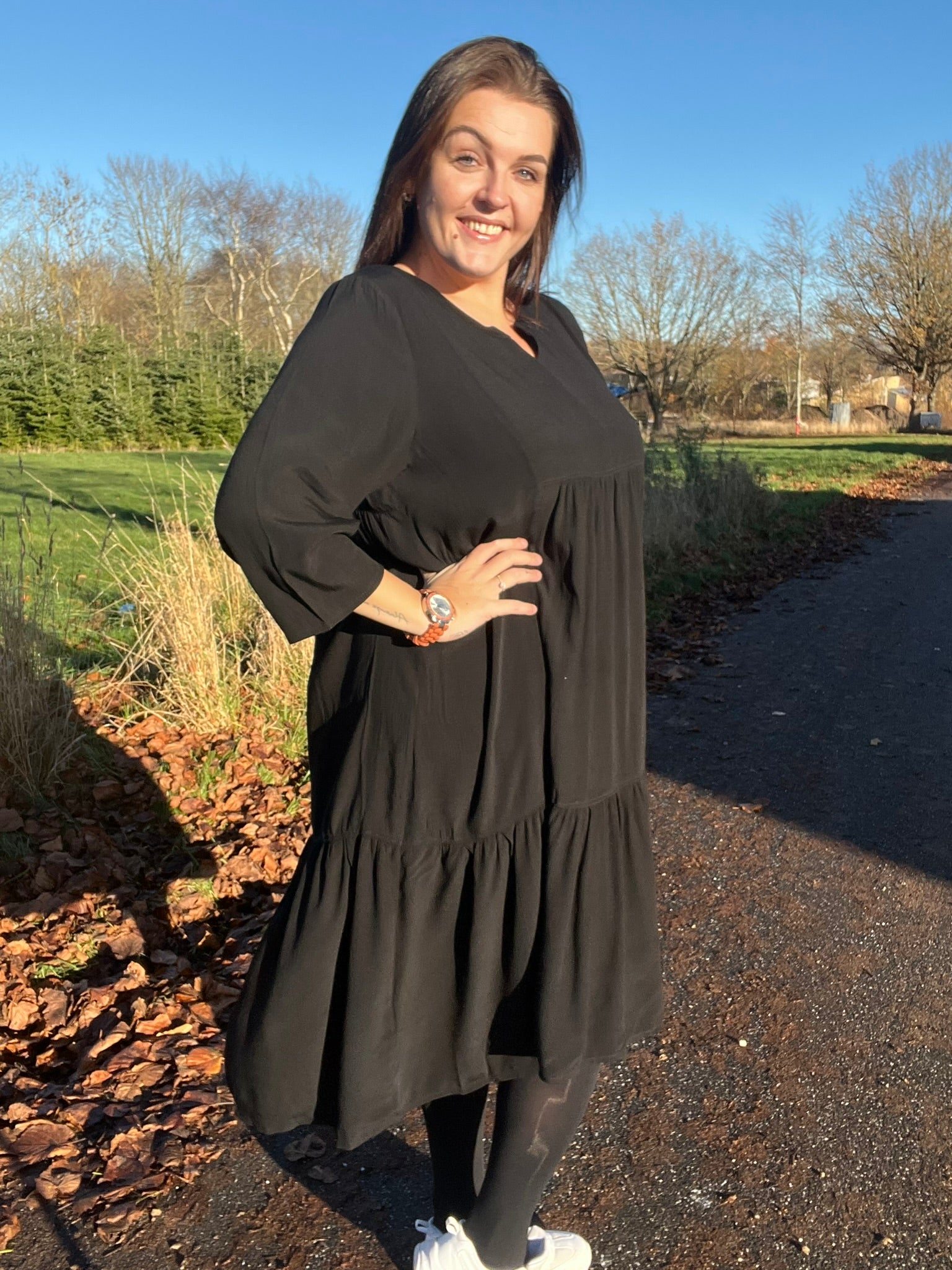 "Rigmor plussize-kjole med flot A-facon, flere lette lag, forlænget ryg og to diskret placerede lommer foran, der virker slankende."