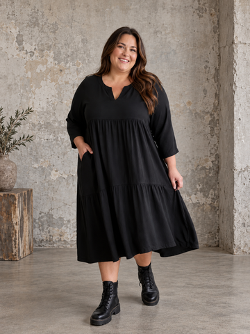 "Rigmor plussize-kjole med flot A-facon, flere lette lag, forlænget ryg og to diskret placerede lommer foran, der virker slankende."