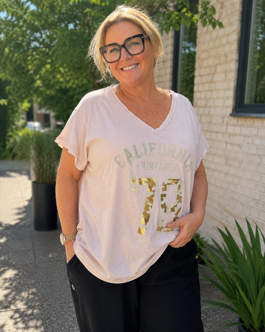 Kate T-shirten er den perfekte hverdagsfavorit med et moderne og afslappet look. Den bløde kvalitet, den flotte V-hals og det trendy California Vintage-print giver et råt udtryk, som er nemt at style til både jeans, hørbukser og shorts.

Den løse pasform falder flot over kroppen uden at stramme og gør T-shirten behagelig at have på hele dagen. De opsmøgede ærmer giver et smart finish, mens det lette materiale gør den ideel til både sommer og som lag under en cardigan eller jakke.

billed er ai generet