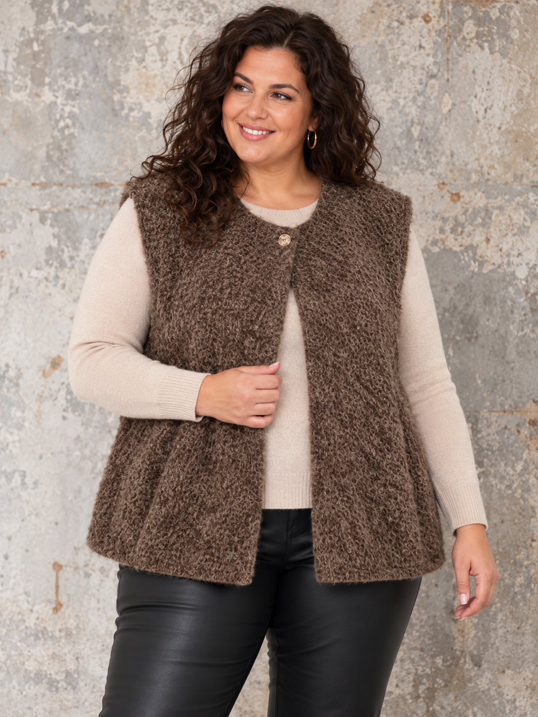 Boucle vest med god pasform og facon til plus size kvinden. Den er perfekt under en strik da ærmegabet har en god størrelse. Den er rund i halsen og spændes med en knap foroven. 

Billedet er genereret vha. AI-teknologi.