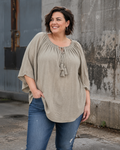 Ella tunika i hvid på plus size-model i størrelse 46/48. Tunikaen er fremstillet i en skøn, blød og let kvalitet med løs pasform, rund hals med bindebånd og dekorative kvaster samt feminine flæseærmer. Den luftige model giver et afslappet og komfortabelt udtryk og er stylet med jeans. Billedet er AI-genereret.