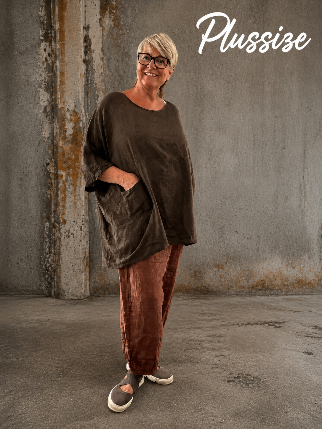 **Alt-tekst – Susanne plussize bomuldstunika (AI-genereret billede):**

AI-genereret billede af en smilende plus-size model iført Susanne bomuldstunika i mørk brun. Tunikaen har en løs, oversize pasform med rund hals, korte brede ærmer og store påsyede lommer foran. Den er stylet med rustfarvede bukser og komfortable sko i et råt industrielt miljø, som fremhæver tunikaens afslappede og moderne udtryk. Ideel til kvinder, der ønsker komfort, bevægelsesfrihed og et stilfuldt hverdagslook.