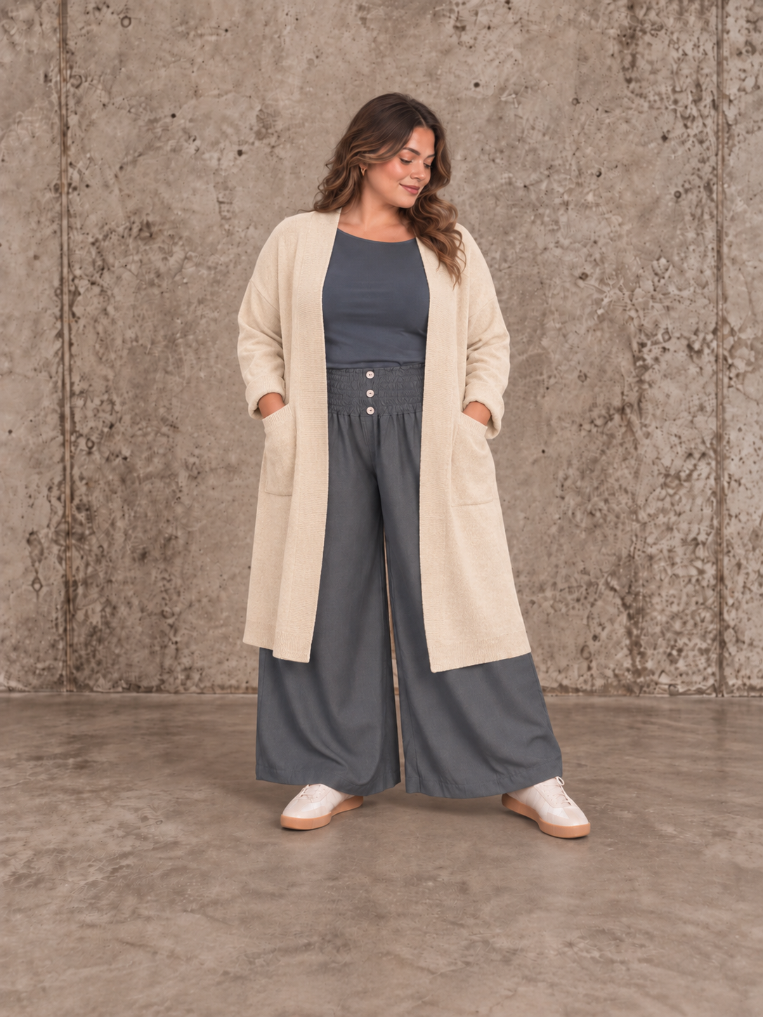 "Model i Tora viddebuks med bred smock-elastik i taljen, dekorative knapper og vide ben. Buksen vises i brun  sammen med en løs camel bluse. Modellen er str. 46/48 og 168 cm høj." billed er ai generet