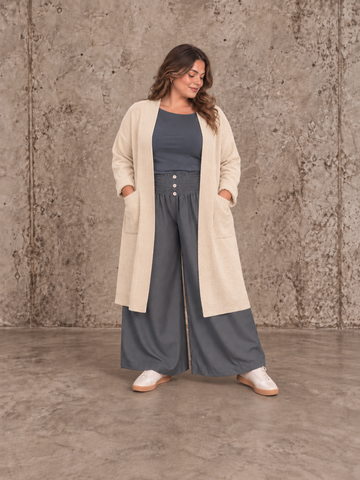 "Model i Tora viddebuks med bred smock-elastik i taljen, dekorative knapper og vide ben. Buksen vises i brun  sammen med en løs camel bluse. Modellen er str. 46/48 og 168 cm høj." billed er ai generet