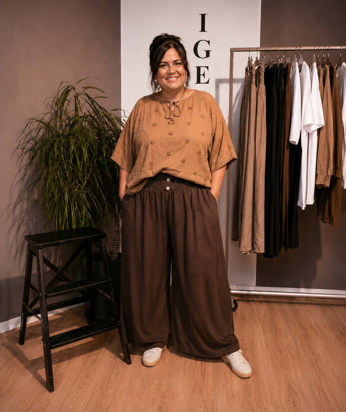 "Model i Tora viddebuks med bred smock-elastik i taljen, dekorative knapper og vide ben. Buksen vises i brun  sammen med en løs camel bluse. Modellen er str. 46/48 og 168 cm høj." billed er ai generet