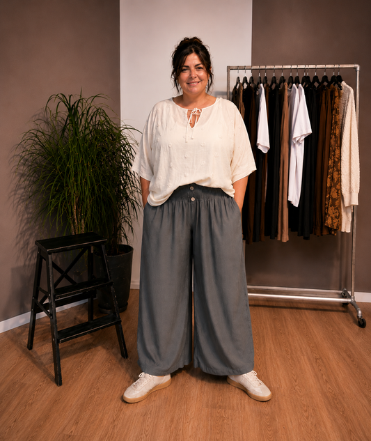 "Model i Tora viddebuks med bred smock-elastik i taljen, dekorative knapper og vide ben. Buksen vises i Grå sammen med en løs beige bluse. Modellen er str. 46/48 og 168 cm høj." Billed er ændret i Ai
