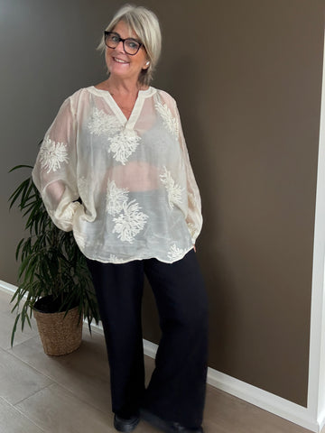 Feminin plus size bluse i en smuk fløde-farve. Den er med broderede blomster, som gør den lidt pyntet.