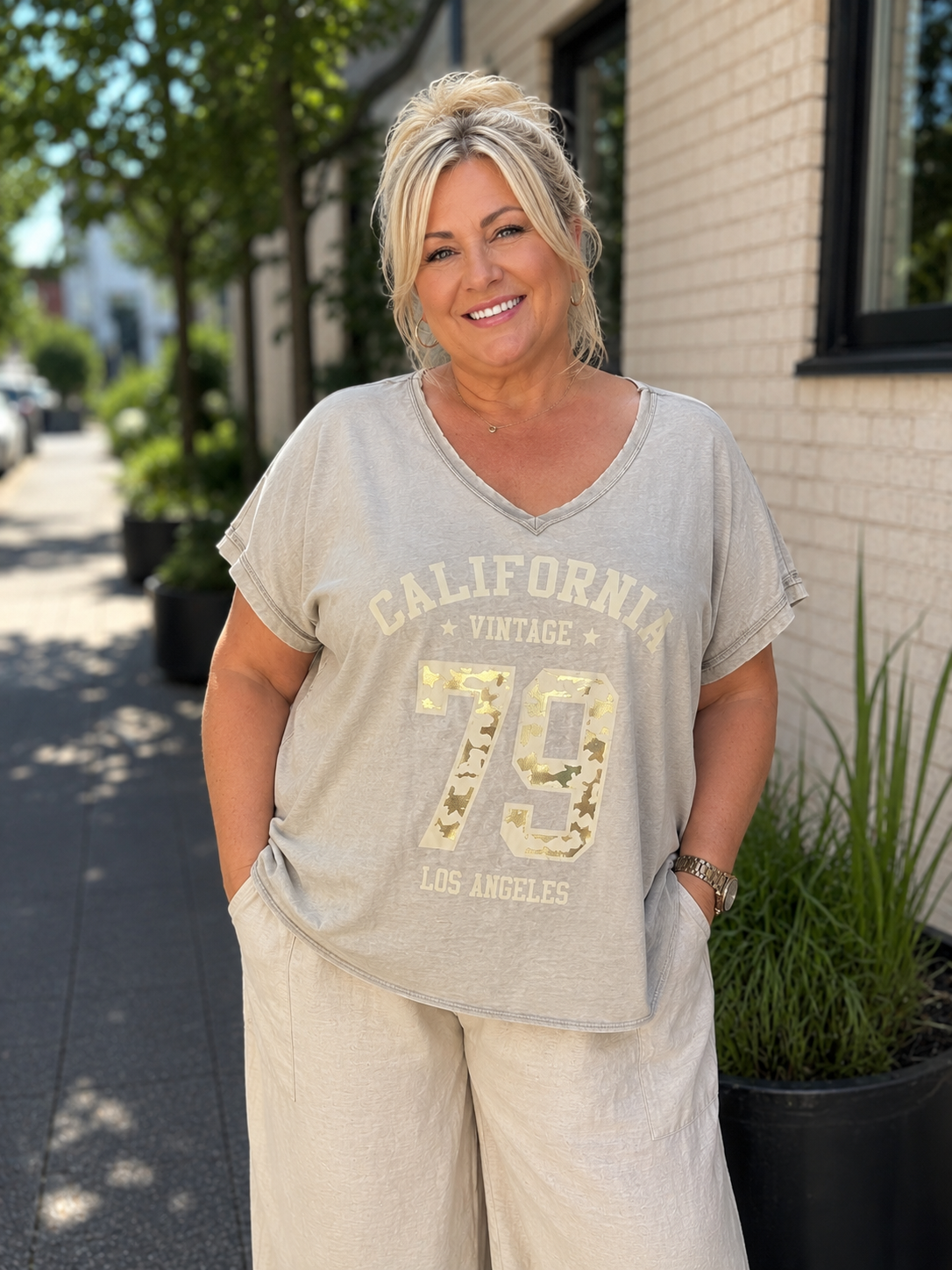 Kate T-shirten er den perfekte hverdagsfavorit med et moderne og afslappet look. Den bløde kvalitet, den flotte V-hals og det trendy California Vintage-print giver et råt udtryk, som er nemt at style til både jeans, hørbukser og shorts.

Den løse pasform falder flot over kroppen uden at stramme og gør T-shirten behagelig at have på hele dagen. De opsmøgede ærmer giver et smart finish, mens det lette materiale gør den ideel til både sommer og som lag under en cardigan eller jakke.

billed er ai generet