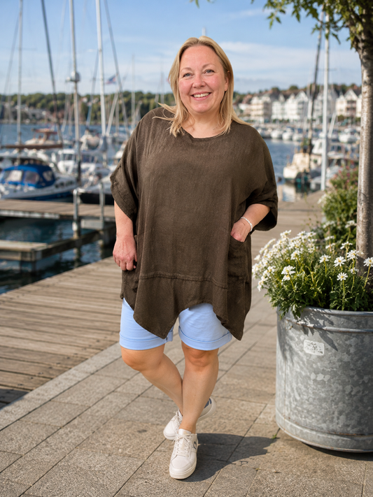 Lene Plus Size tunika i blød og let kvalitet med en flot, afslappet pasform. Tunikaen har rund hals, korte ærmer med opsmøg, praktiske lommer og en asymmetrisk kant, der falder smukt. Den løse facon gør den behagelig at have på og nem at style med både bukser, shorts og leggings. Fås i flere flotte farver og passer perfekt til plus size kvinder, der ønsker komfort og moderne stil.ai generet billed.
