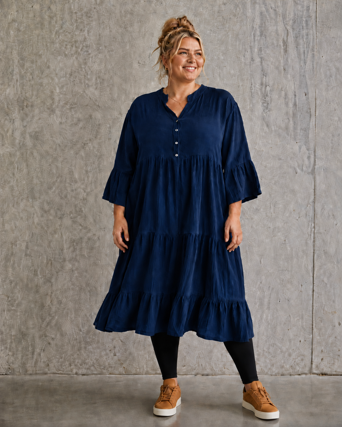 Ella plus size kjole i mørk marineblå med V-hals, knapper, 3/4 ærmer og flot vidde – stylet med sorte leggings og karamel sneakers.
Billed er ai generet