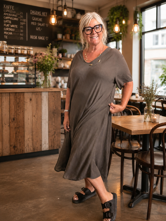 “Pernille plussize viskose kjole i smuk A-facon. Modellen er 168 cm høj og bruger størrelse 46/48. Kjolen har korte ærmer, V-udskæring og et løstsiddende, flatterende fald i en varm camel farve.”billed er Ai generet